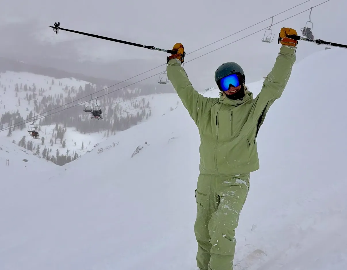 Emersyn on skis with her poles raised on a snowy ridge